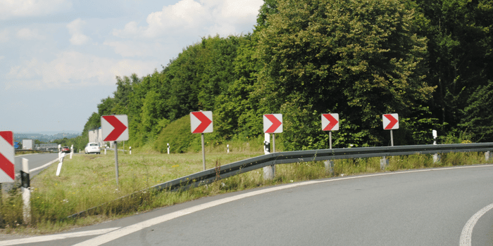 Kavisli bir yolda hız uyarısı veren kırmızı beyaz trafik levhaları